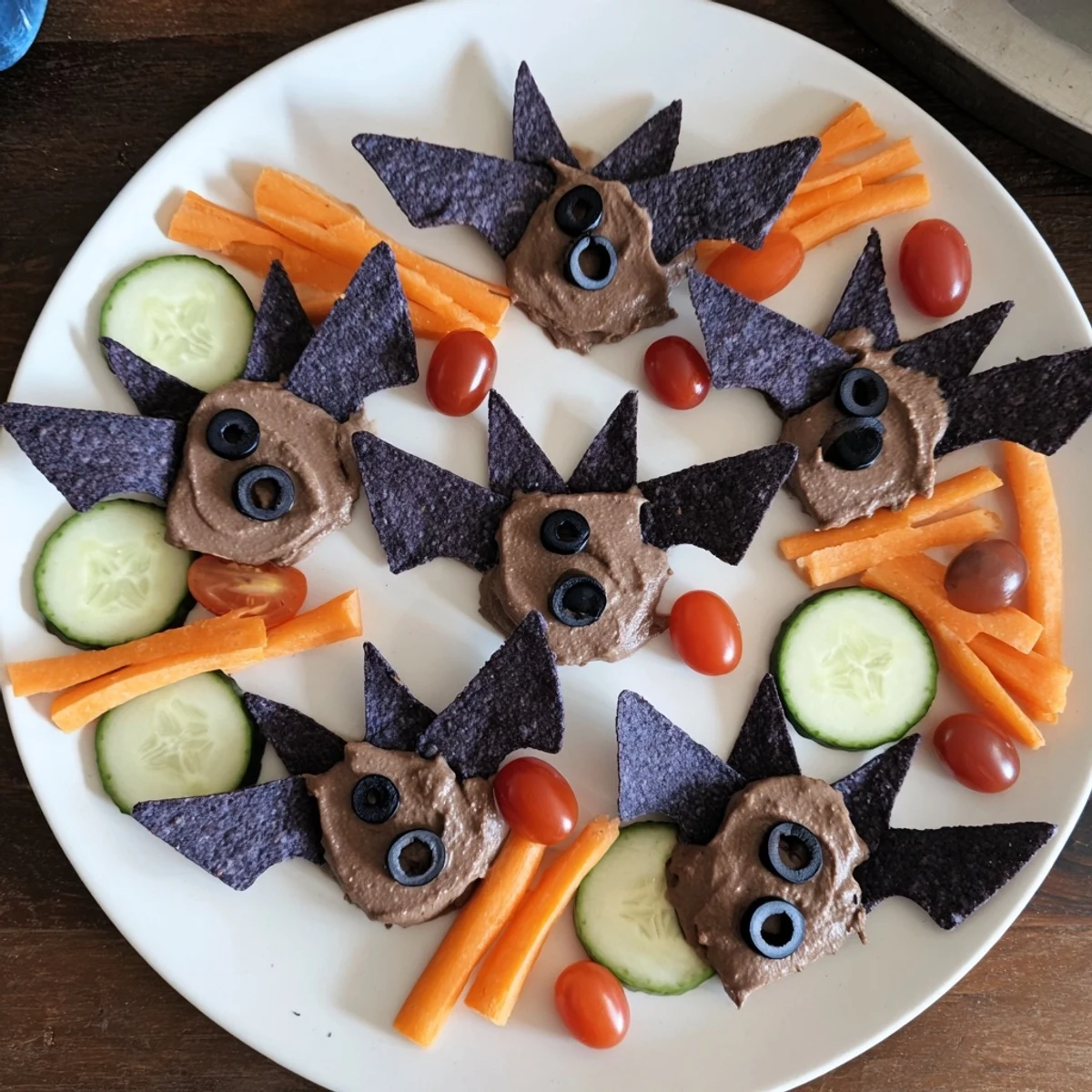 Spooky Bat Bean Dip Platter with black bean bats, vibrant veggies, and tortilla chips for Halloween appetizer.