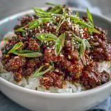Overhead view of a Korean Beef Bowl with vibrant quick-pickled carrots and radishes, green onions, and sesame seeds, arranged neatly on a white plate.