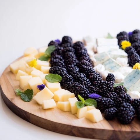 A beautifully arranged yin-yang balance appetizer board with blackberries, cheeses, and fruits.