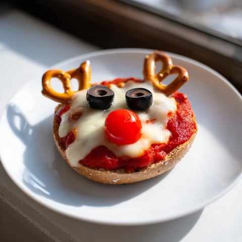 Delicious Reindeer Face Pizza Bagels with melted cheese, olive eyes, and pretzel antlers.