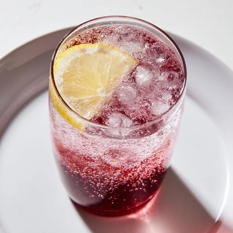 A refreshing Sleepy Girl Mocktail, a vibrant, ruby-red drink with a lemon twist and ice.
