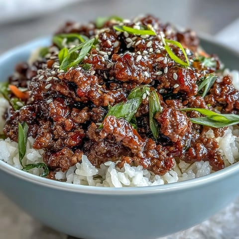 A close-up of a Korean Beef Bowl showing seasoned ground beef with gochujang sauce, served over fluffy rice and topped with crisp cucumber and tangy kimchi.